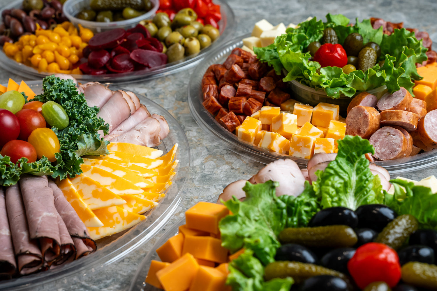 Vegetable platters, charcuterie boards and a variety of platters for catering events displayed on a table.